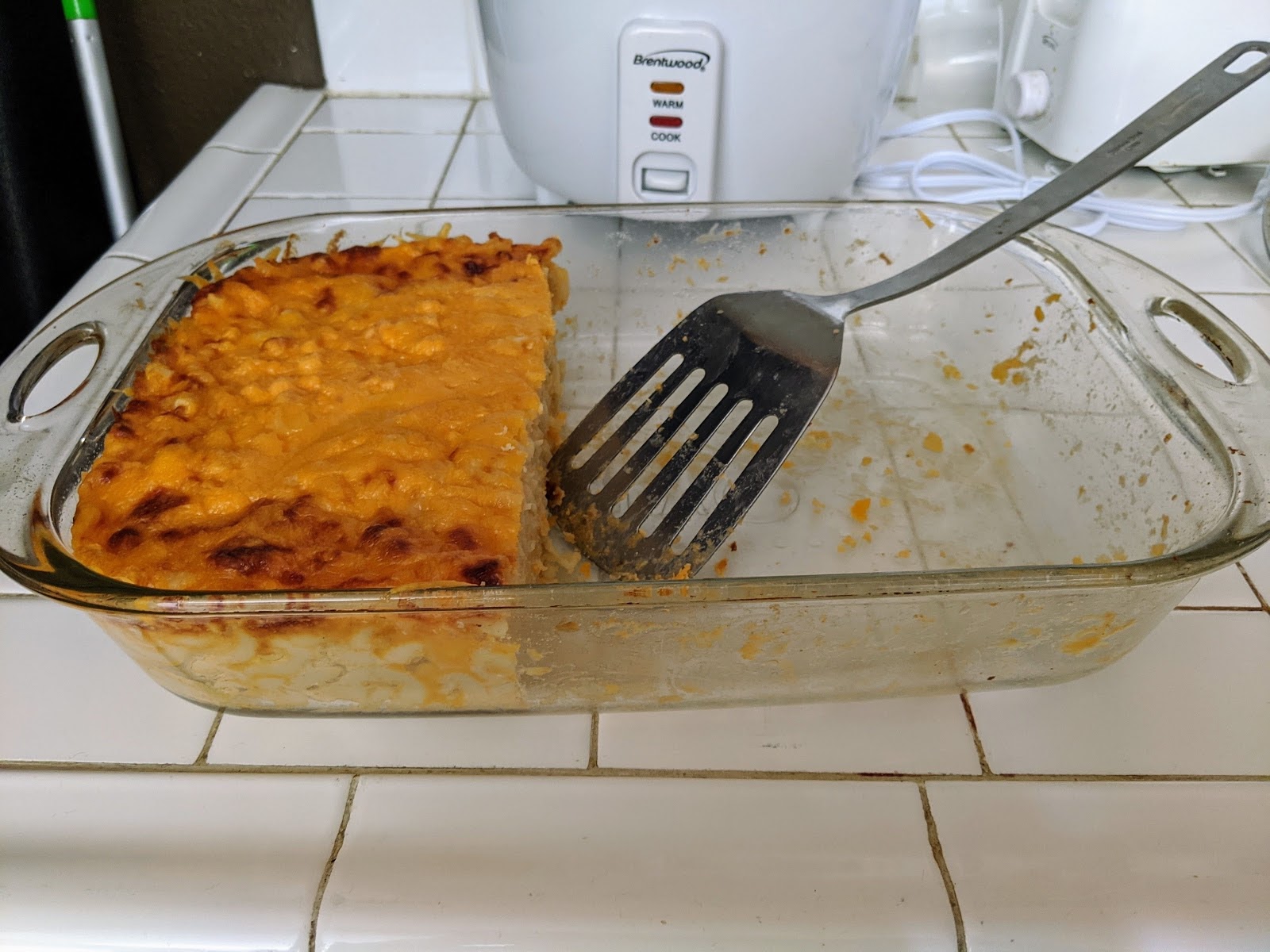 Photograph. Mac and cheese in pan with spatula. Less than 1 half remains.