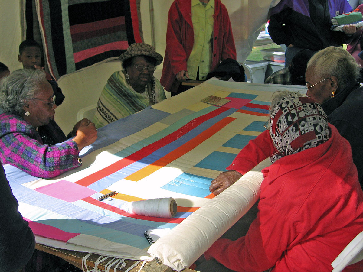 Photograph of ladies sewing a blanket made of shapes.