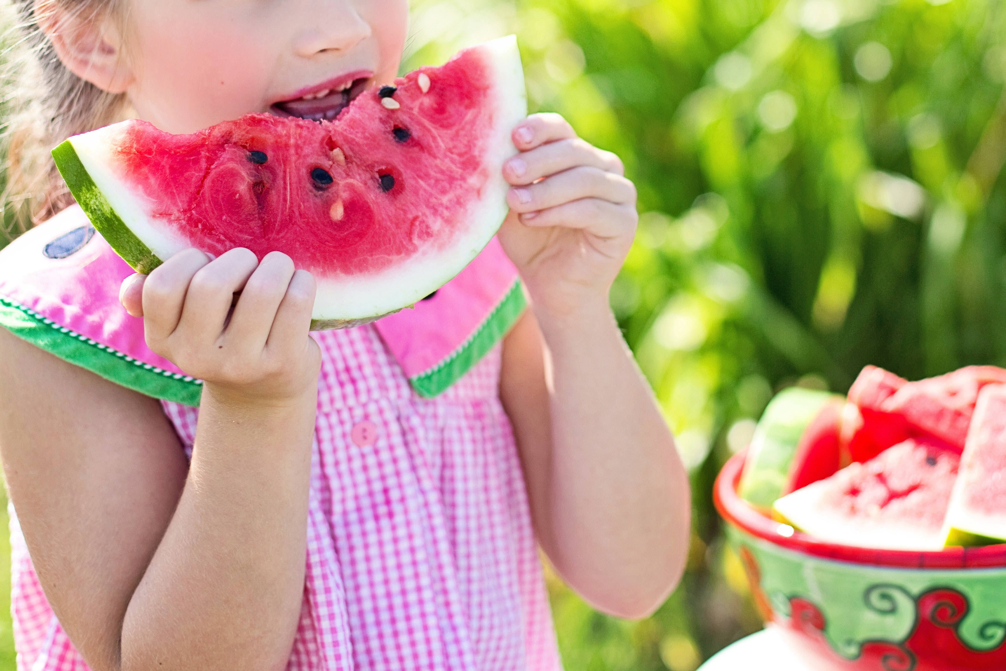 little girl in watermelon sun dress eating a slice of watermelon