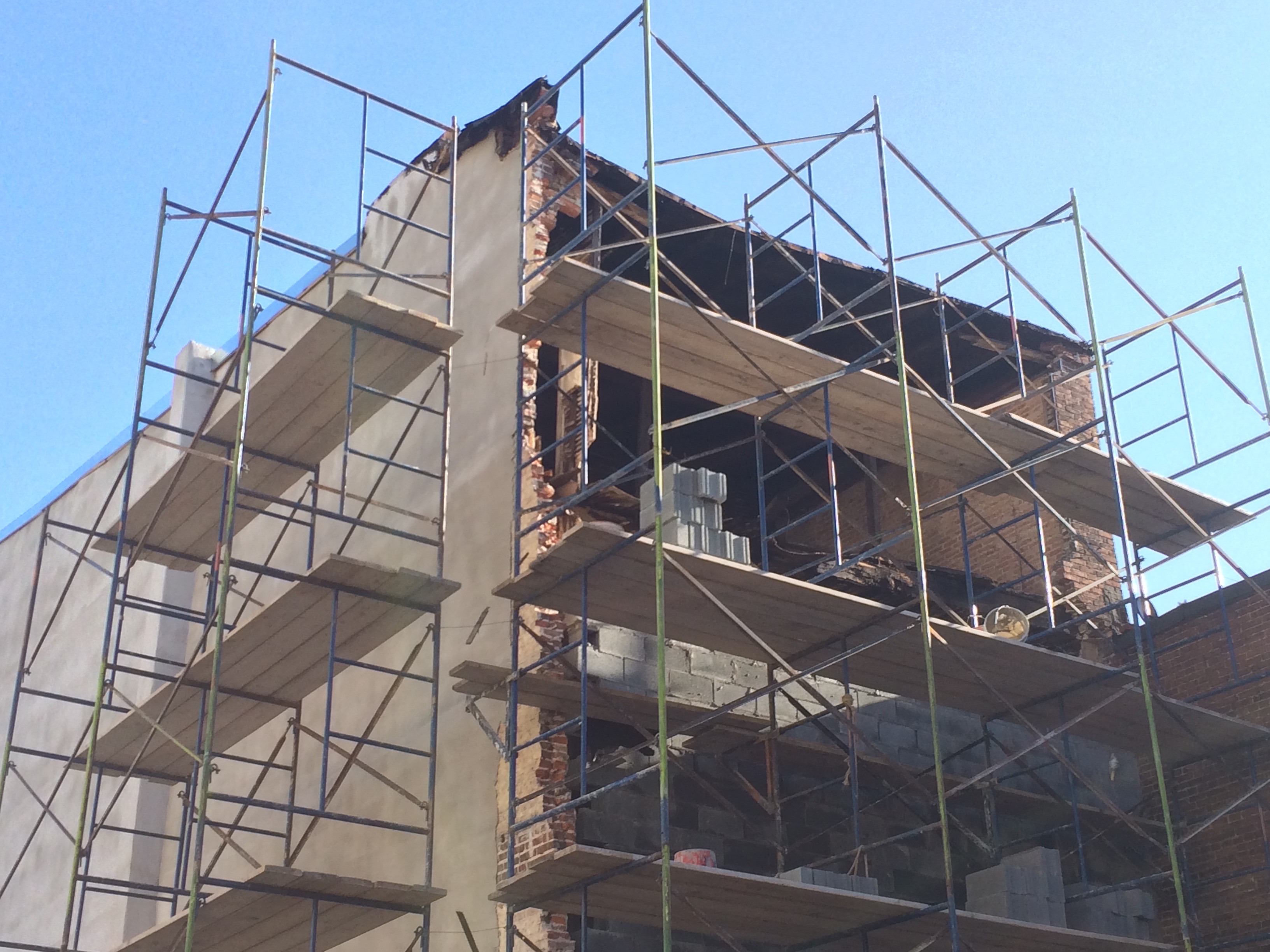 A photo of scaffolding around a building. 3 stories of scaffolding are visible. One side of scaffolding has 4 vertical posts, with three sets of diagonal posts creating an X across each floor.