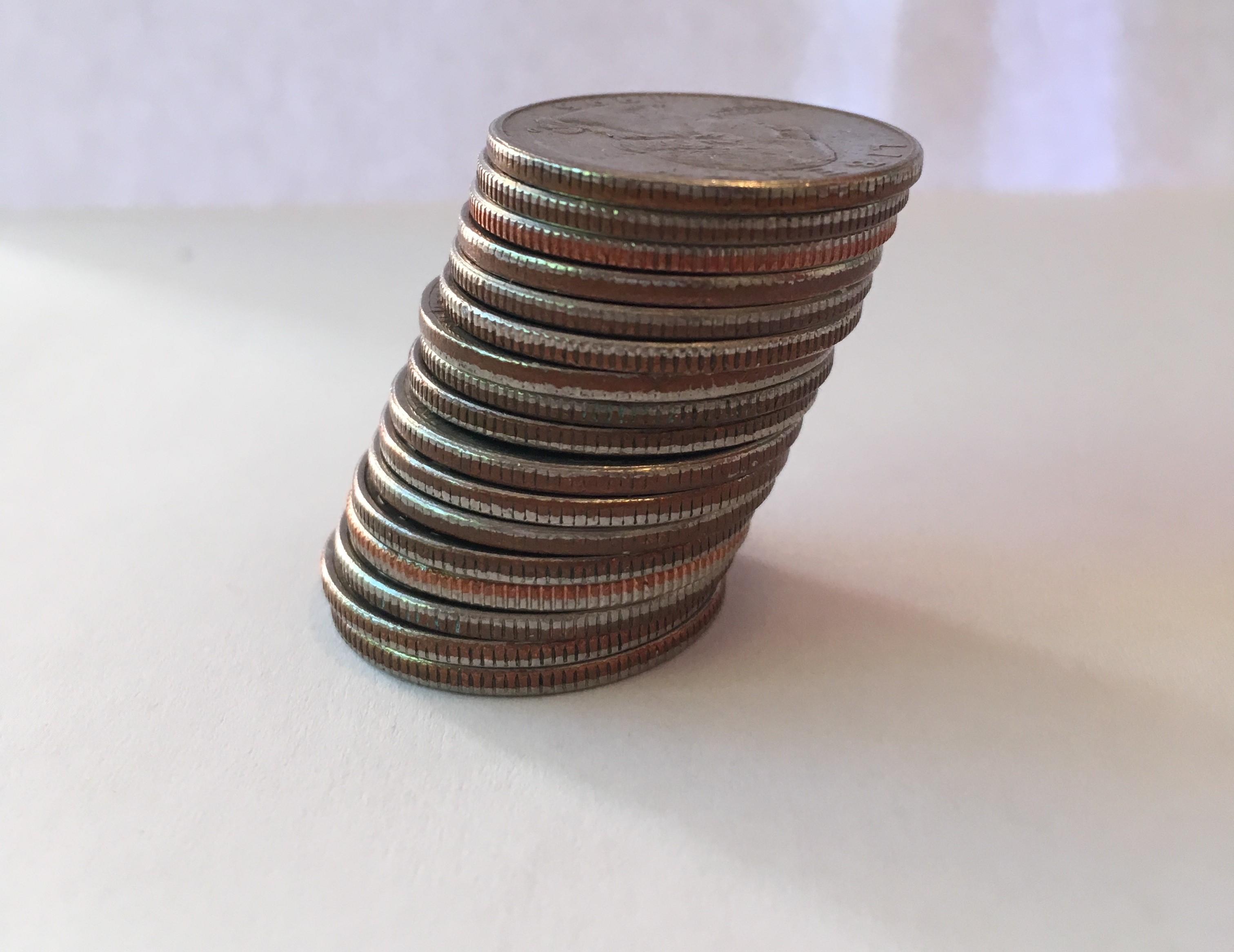 A photo of a stack of coins, quarters, each one slightly off center from the one below it so that the stack appears to be leaning.