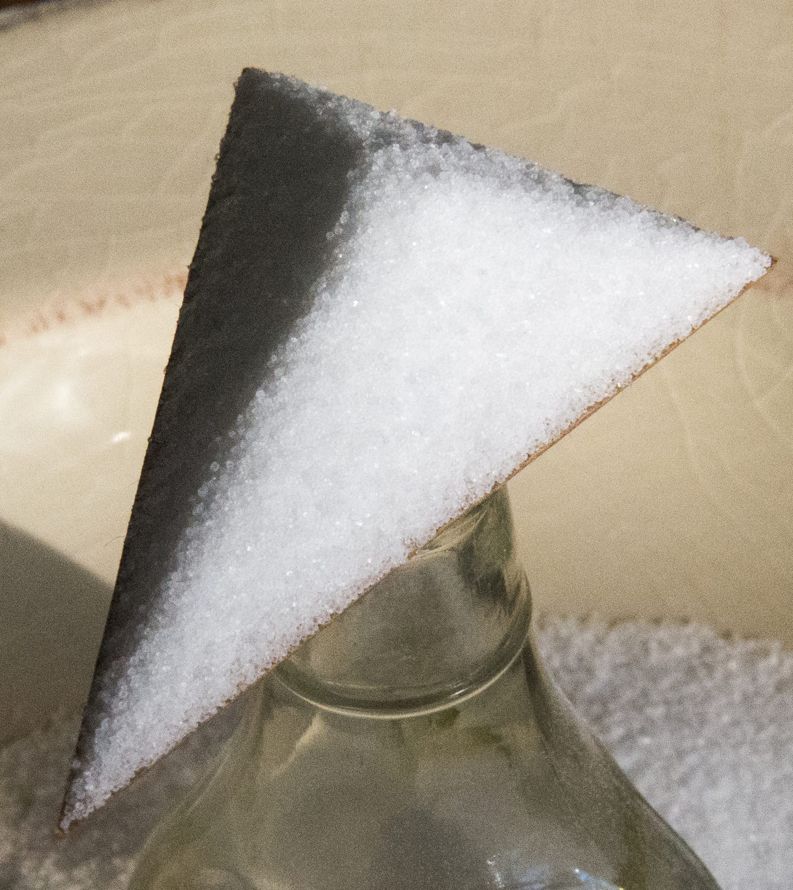 Cardboard triangle on top of glass bottle, with salt on top of triangle.