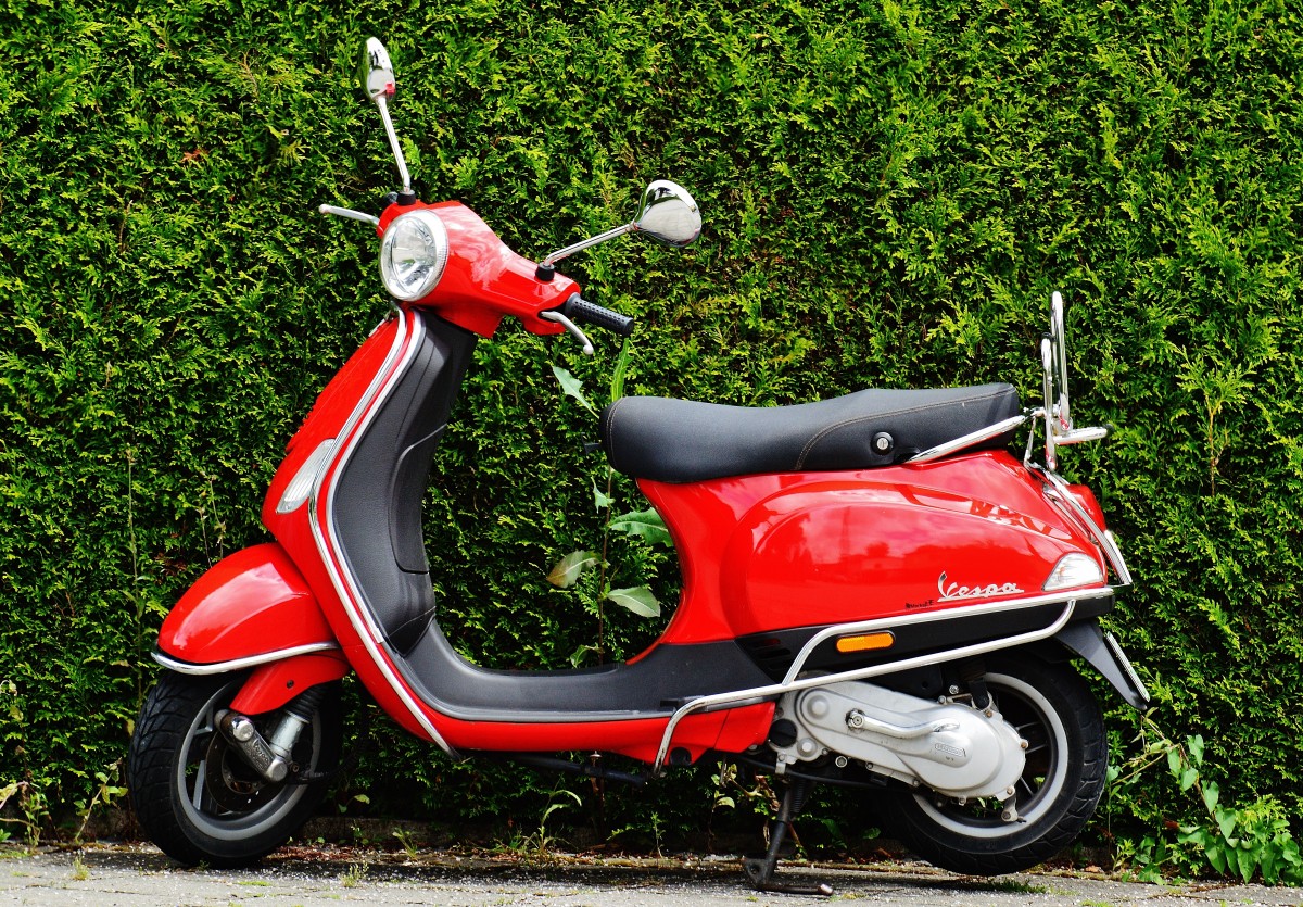 Red scooter in front of bushes.