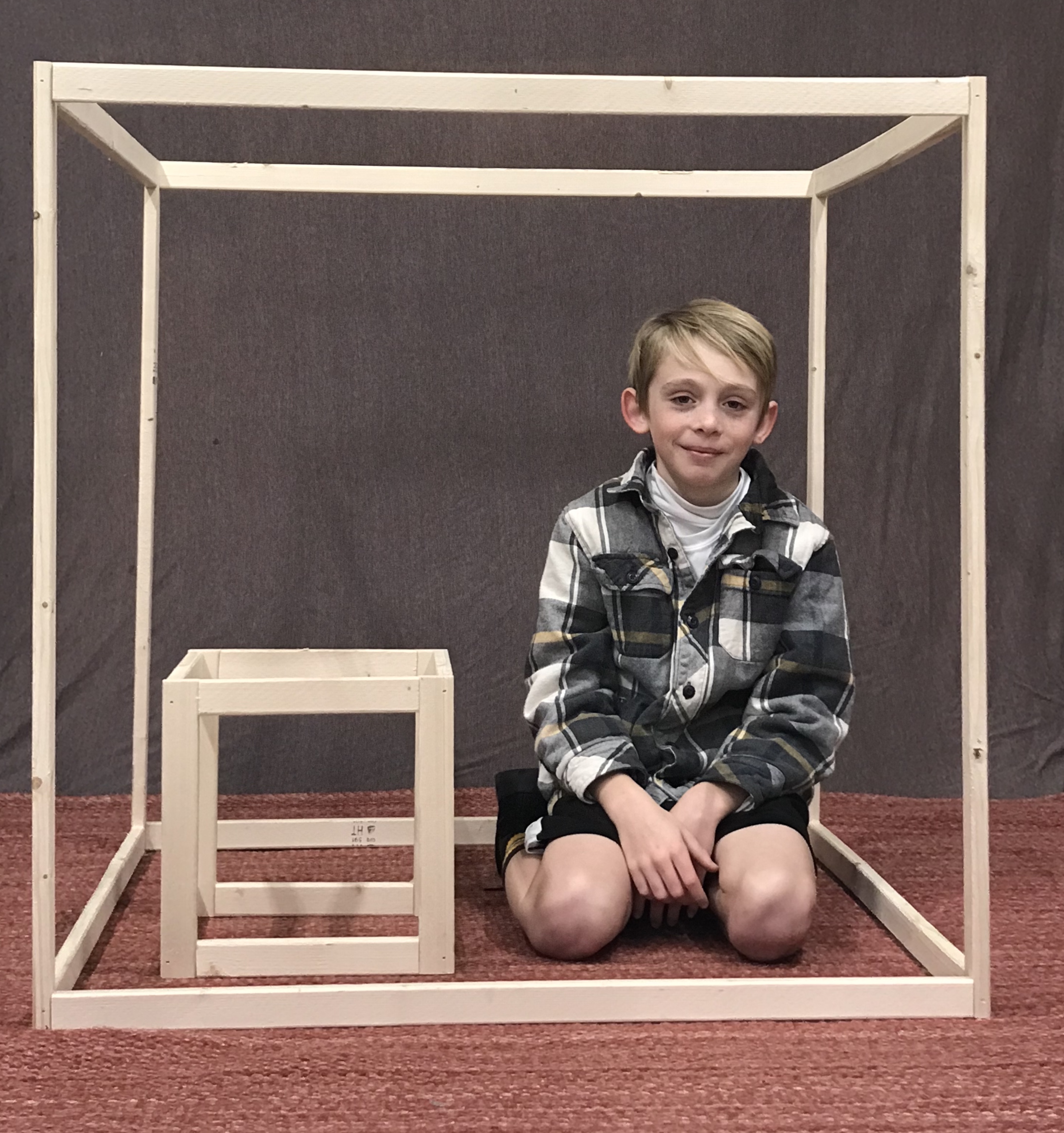 A student and two rectangular prisms. . The student is sitting inside the large rectangular prism and is next to the smaller prism.