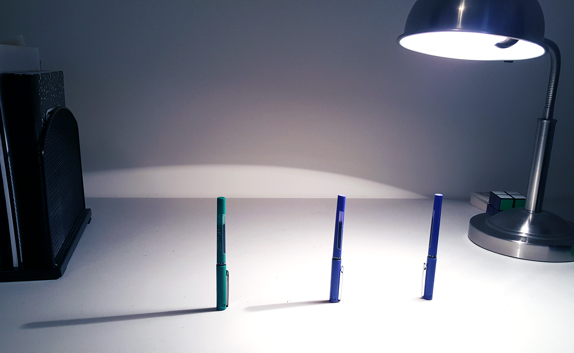 Photograph of 3 pens standing upright. Lamp on right. Longest shadow formed by pen on far left, shorter shadow on middle pen, no shadow on pen on right.