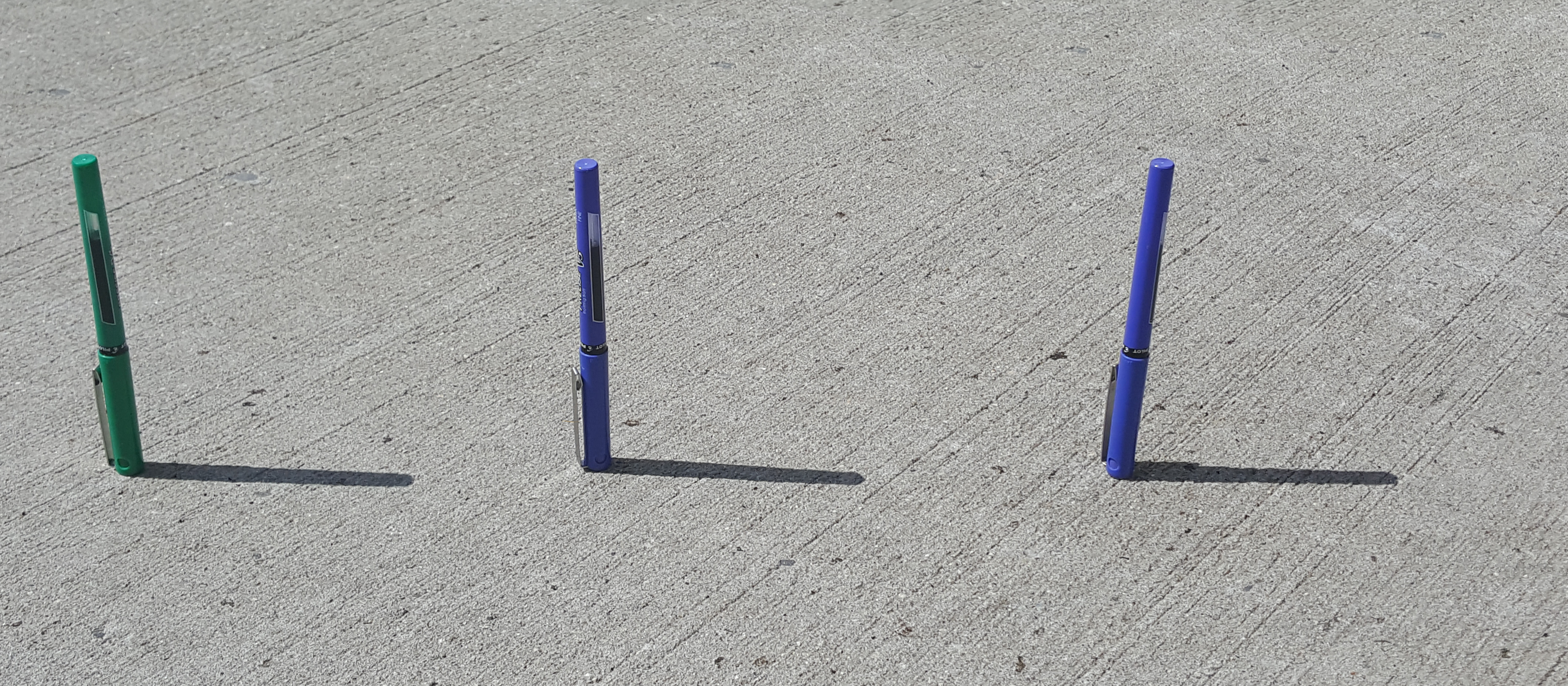Photograph of 3 pens standing upright forming shadows on the desk