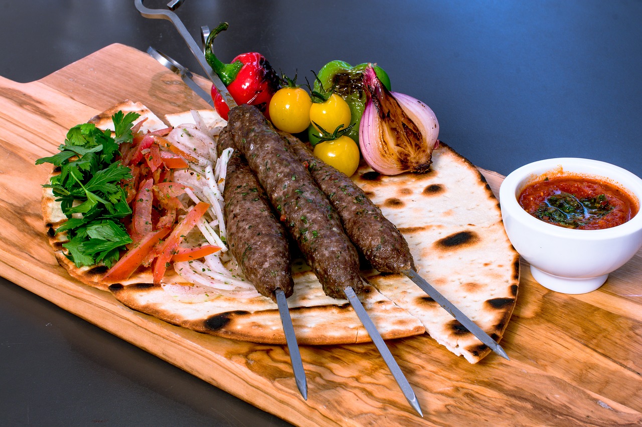 Skewers of meat and piles of vegetables on top of pita bread, sauce on side