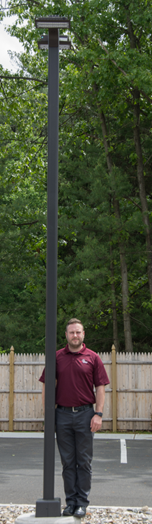 Image of six foot adult man next to lamp post. Lamp post is taller than man.