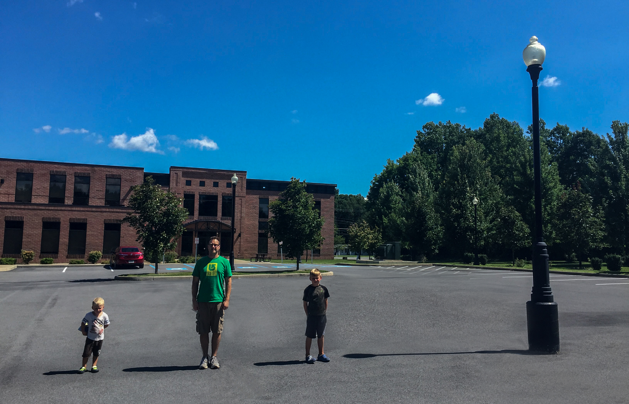 Photograph of 2 boys, a man, and a lamp post, each have a shadow to their left.