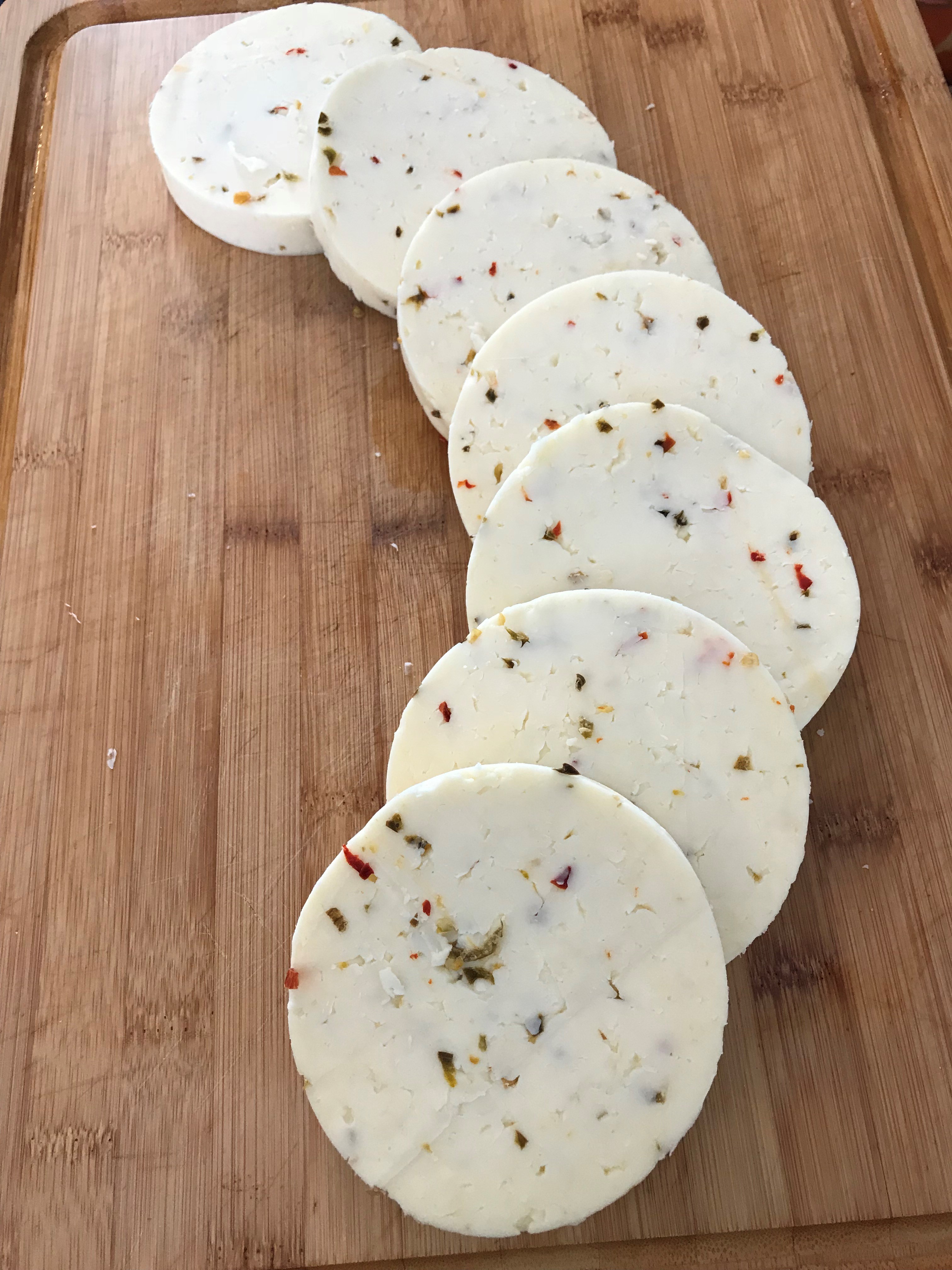 Image of slices of cylindrical cheese spread out on a wooden cutting board.
