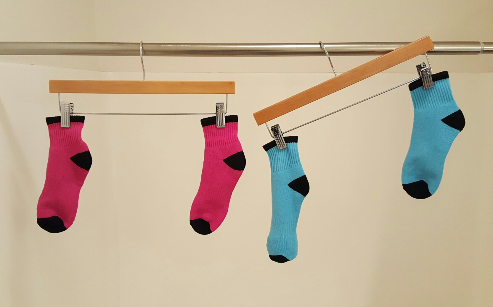 Two clothes hangers hanging from a rod. Two pink socks, level. Two blue socks, not level.