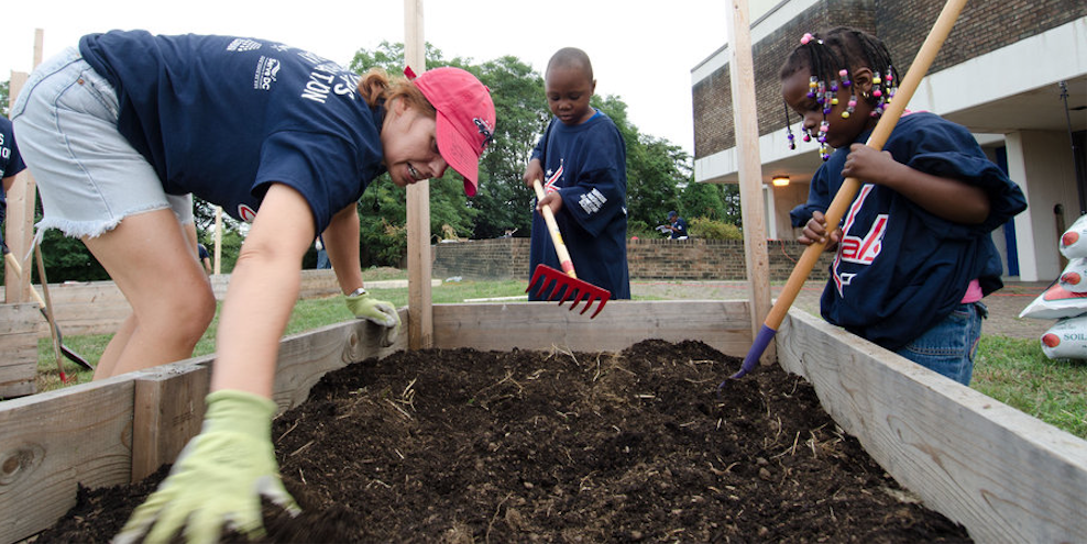 One adult and two children filling an outdoor square planter with soil