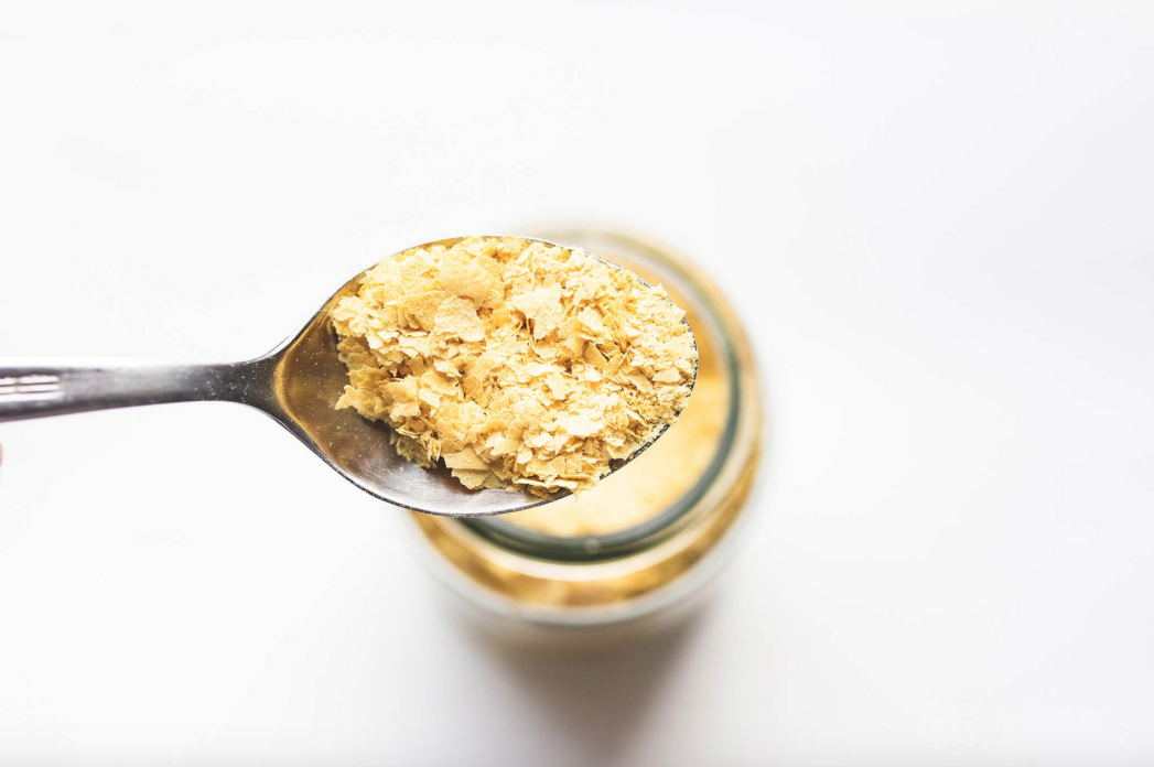 Spoon of vegan nutritional yeast flakes on white background